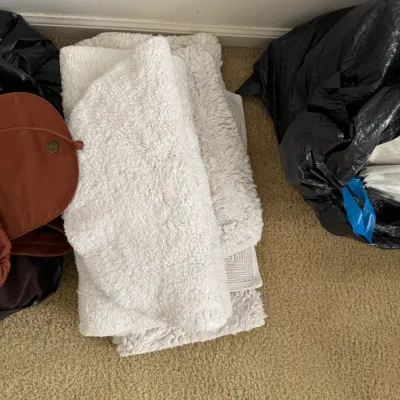 Stack of plush white bath mats and rugs, shown folded on a carpeted floor next to storage bags.