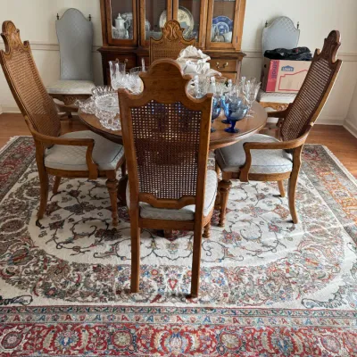 Sale Photo Thumbnail #115: Vintage dining set featuring a round wooden table, cane-back chairs with upholstered seats, and a matching china cabinet, displayed on a traditional patterned area rug.