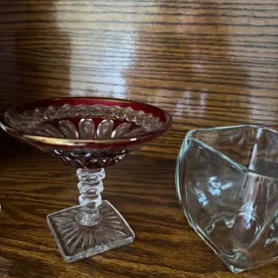 Sale Photo Thumbnail #164: Vintage ruby-stained glass compote with a clear pedestal base alongside a small, clear glass bowl, displayed on a wooden shelf.