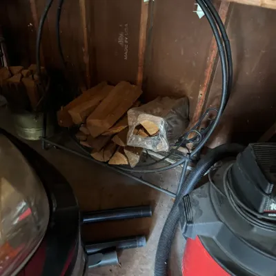 Black metal hoop firewood rack holding split logs, shown alongside a red wet/dry shop vacuum in a garage setting.