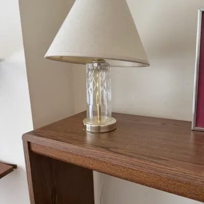 Vintage crystal cylinder table lamp with brass accents and a cream-colored fabric shade, resting on a wooden shelf.