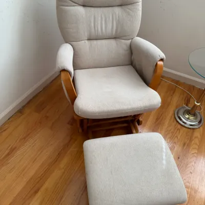 Upholstered glider rocker and matching ottoman with light beige fabric and a natural wood frame.