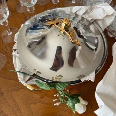 Sale Photo Thumbnail #105: Polished stainless steel or silver-plated chafing dish lid featuring a decorative gold-tone branch and leaf handle, surrounded by glassware.