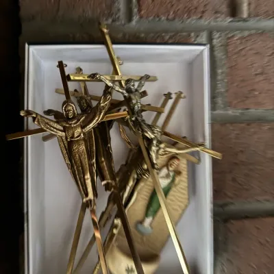 Sale Photo Thumbnail #175: Collection of vintage brass and metal crucifixes and religious figurines, displayed in a white box.