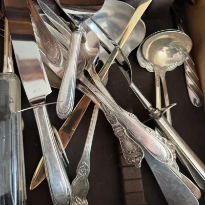Assorted vintage silver-plated and stainless steel serving utensils, including a cake server, ladles, and serving knives, stored in a...