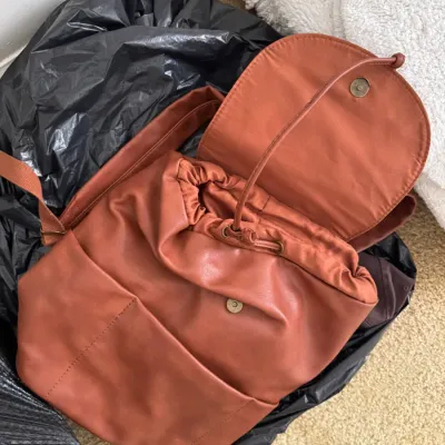 Terracotta faux-leather drawstring backpack featuring a magnetic snap closure and front slip pocket.