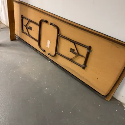 Vintage folding banquet table with a wood-look laminate top and brown metal folding legs, showing some wear from use.