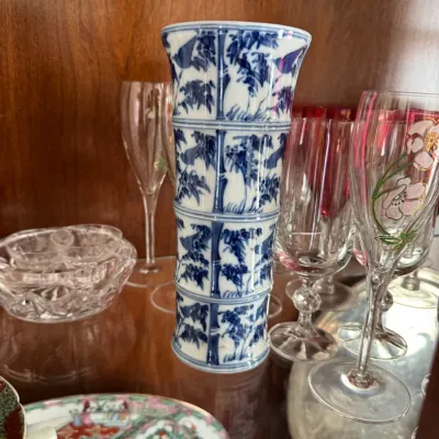 Vintage blue and white porcelain vase with a bamboo-style segmented design, displayed alongside assorted crystal and glassware in a...