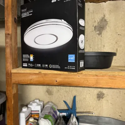 Artika Horizon LED ceiling light fixture in its original box, displayed on a wooden shelf alongside various household and maintenance...