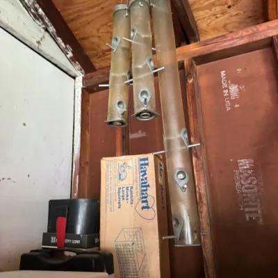 Three vintage Droll Yankees tube bird feeders hanging in a shed, showing some weathering and discoloration from outdoor use.
