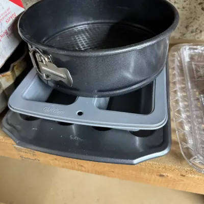 Stack of non-stick baking pans, including a dark grey springform pan and two Wilton baking sheets, showing light signs of use.