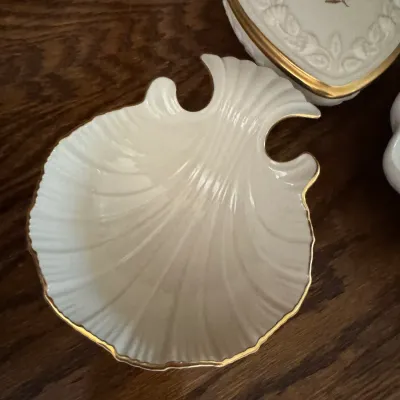 Lenox ivory porcelain shell-shaped dish with gold trim, shown alongside a heart-shaped trinket box on a wooden surface.