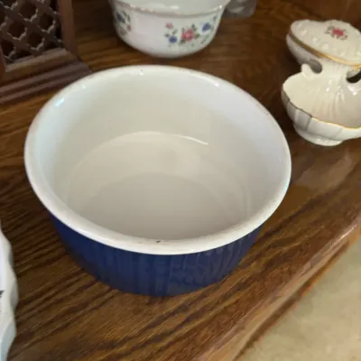 Sale Photo Thumbnail #190: Cobalt blue ribbed ceramic ramekin or baking dish with a white interior, displayed on a wooden shelf alongside other vintage porcelain pieces.