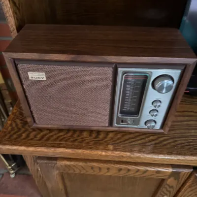 Sale Photo Thumbnail #181: Vintage Sony table radio with a wood grain cabinet, woven speaker grille, and silver-toned control panel, circa 1970s.