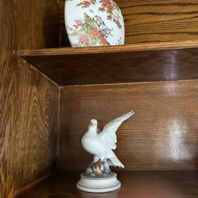 Sale Photo Thumbnail #184: Vintage porcelain dove figurine on a pedestal base, shown alongside an Asian-style floral ceramic vase on wooden shelving.