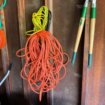 Assorted garden tools and extension cords, including a pair of long-handled loppers with green grips and a bundle of orange and yellow...