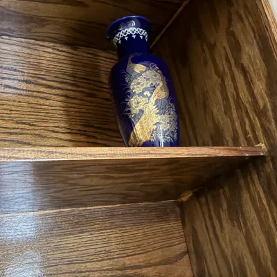 Sale Photo Thumbnail #148: Cobalt blue ceramic vase featuring a gilded peacock and floral design, displayed on a wooden shelf.