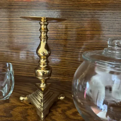 Sale Photo Thumbnail #162: Vintage polished brass candlestick holder featuring a baluster stem and a tiered triangular base with claw feet.