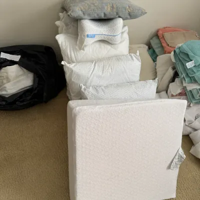 Assorted bed pillows, orthopedic support pillows, and folded linens displayed on a carpeted floor.
