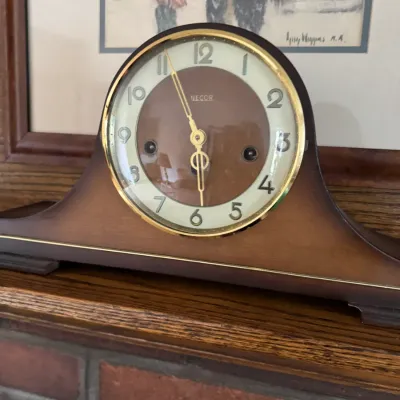 Sale Photo Thumbnail #178: Vintage Necor mantel clock featuring a wooden tambour-style case with gold-tone trim and a two-tone brown and cream face.
