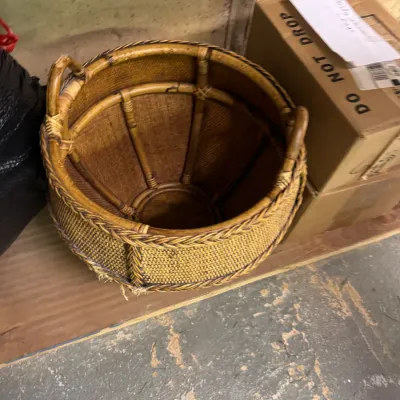 Vintage woven rattan and bamboo basket with integrated side handles, showing some wear along the bottom edge.