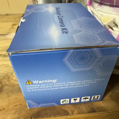 Backup Camera Kit in its original blue cardboard box, showing warning labels and shipping icons.