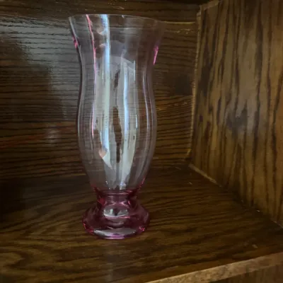 Sale Photo Thumbnail #193: Vintage pink depression glass hurricane vase with a pedestal base, displayed on a wooden shelf.
