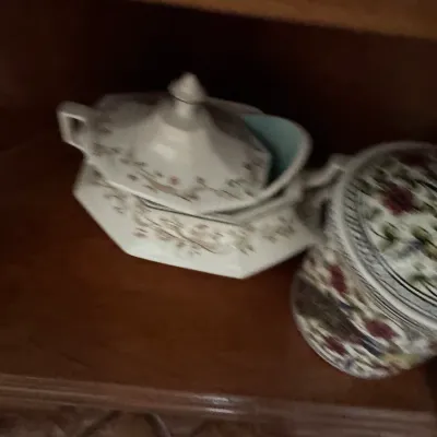Vintage ceramic tureen with a matching lid and floral pattern, displayed alongside a decorative floral canister on a wooden shelf.