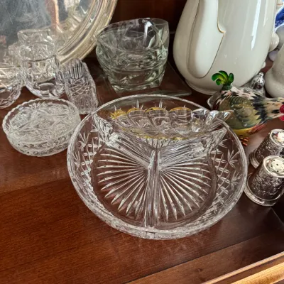 Sale Photo Thumbnail #139: Vintage cut glass serving dishes, including a three-part divided relish dish, alongside a white porcelain teapot with gold trim and other decorative tabletop items.