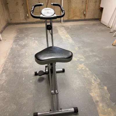 Folding magnetic upright exercise bike with an adjustable padded seat, digital monitor, and tension control knob.