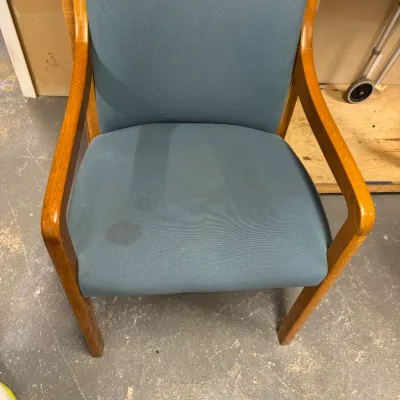 Mid-century modern style wooden armchair featuring blue fabric upholstery on the seat and backrest, showing some minor staining on the...