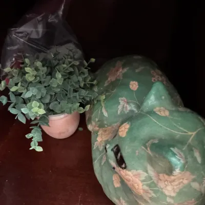 Sale Photo Thumbnail #101: Vintage green ceramic sleeping cat figurine with a floral chintz pattern, displayed next to a small faux potted plant.
