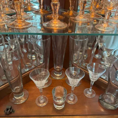 Sale Photo Thumbnail #120: Assorted glassware collection including tall pilsner glasses, stemmed cordial glasses, and amber-tinted goblets displayed in a mirrored curio cabinet.