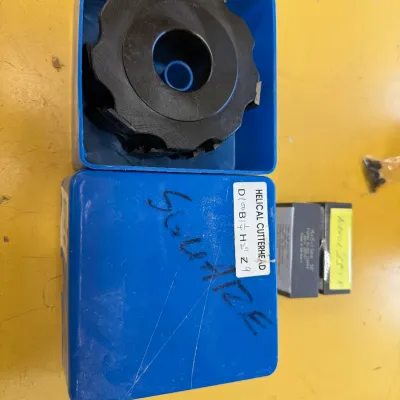 Helical cutterhead for woodworking machinery, shown in its blue plastic storage case alongside its lid and smaller accessory boxes.