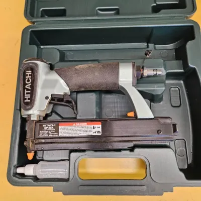 Hitachi NP 35A 1-3/8" pin nailer, showing some wear from use, housed in its original green plastic carrying case with a small bottle...