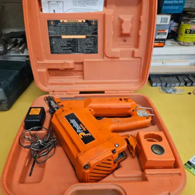Paslode Impulse cordless framing nailer with charger and manual, housed in its original orange hard plastic carrying case.