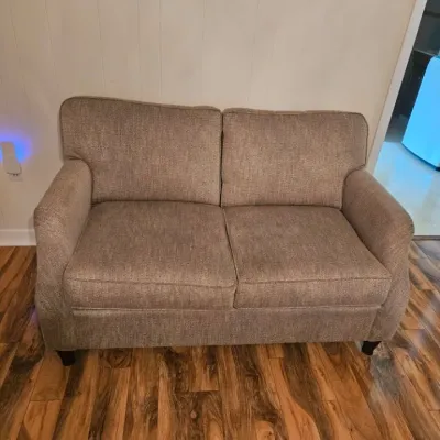 Contemporary two-seater loveseat upholstered in a textured beige fabric, featuring rolled arms and dark wood legs.