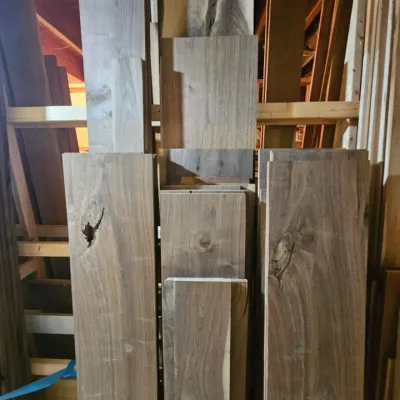 Assorted stacks of rough-cut walnut lumber in various lengths and widths, showing natural grain patterns and knots.