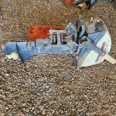 Vintage Evinrude outboard boat motor, showing signs of wear and use, resting on a gravel surface.