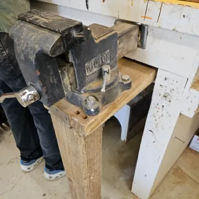 Vintage Wilton bullet vise mounted on a wooden workbench, showing some wear and dust from workshop use.
