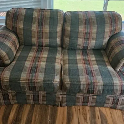 Vintage plaid loveseat featuring a green, red, and beige tartan pattern with rolled arms and a skirted base.