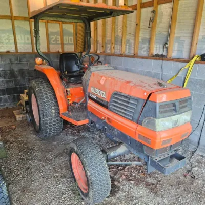 Kubota L2900 utility tractor with a protective canopy, turf tires, and orange finish, showing some wear from use.