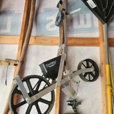 EarthWay Precision Garden Seeder, model 1001-B, hanging on a wall alongside other garden tools.