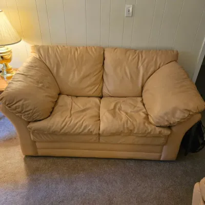 Plush tan leather loveseat with overstuffed cushions, showing some wear consistent with age and use.