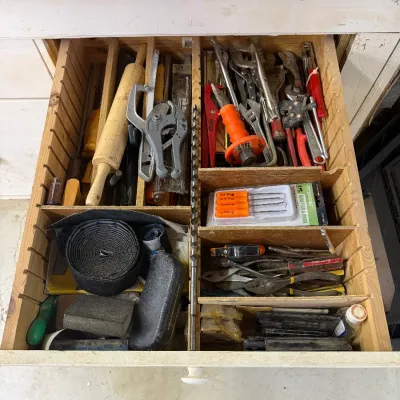 Assorted hand tools, hardware, and workshop supplies organized in a wooden drawer with dividers.