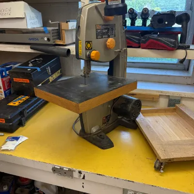 Ryobi benchtop band saw with an attached work light, sitting on a yellow workbench alongside various power tools and workshop supplies.