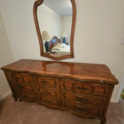 French Provincial style triple dresser with a matching wall mirror, featuring a high-gloss wood grain finish, ornate brass pulls, and...