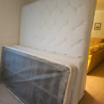 White tufted mattress and matching box spring set, shown standing on end in a hallway.