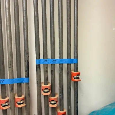 Collection of heavy-duty metal pipe clamps with orange-painted sliding jaws, bundled with blue painter's tape.