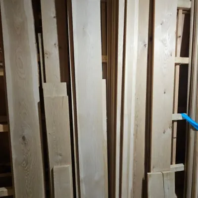 Assorted unfinished hardwood lumber planks of varying lengths and widths, stored vertically in a workshop.